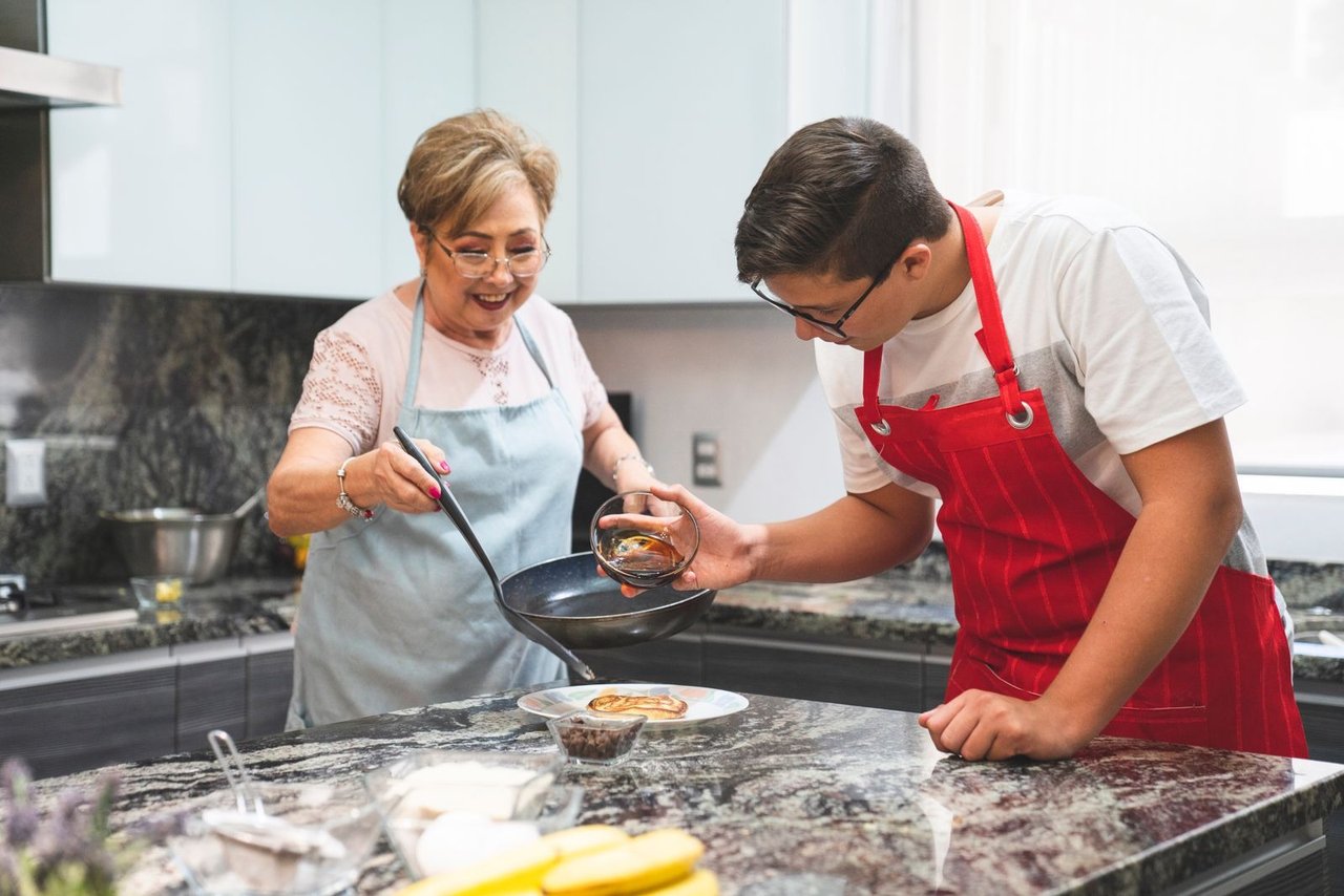 An older woman and a younger man cook together at a kitchen bench.